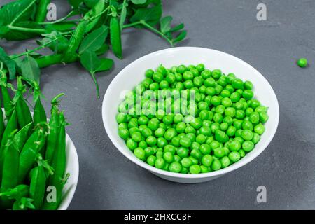 Healthy food. Fresh green peas in a white bowl with leaves and sweet pea pods on a gray background Stock Photo