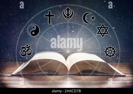 Open book on wooden table with religious symbols and universe background. Concept of the study of religions. Front view. Stock Photo