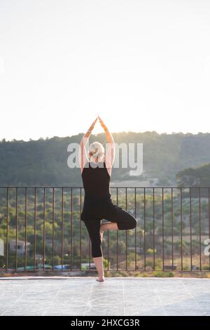 Woman practicing yoga outdoors with view of valley Stock Photo