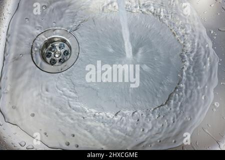 Water flows from a faucet into a sink Stock Photo