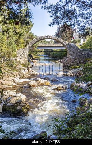 The remains of the Old Packhorse Bridge built in 1717 and the more modern road bridge over the River Dulnain in the village of Carrbridge, Highland, S Stock Photo