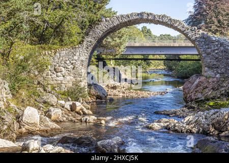 The remains of the Old Packhorse Bridge built in 1717 and the more modern road bridge over the River Dulnain in the village of Carrbridge, Highland, S Stock Photo