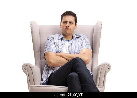 Young man with an angry face sitting in an armchair isolated on white background Stock Photo