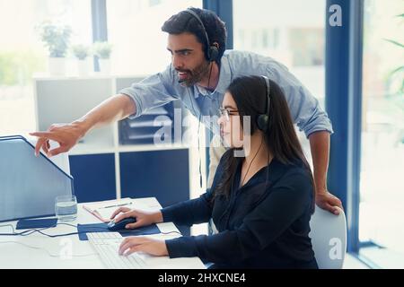 Training a new employee about delivering quality service. Cropped shot of two call centre agents working together in an office. Stock Photo