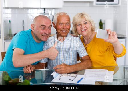 Senior male and female with son taking selfie on mobile phone Stock Photo