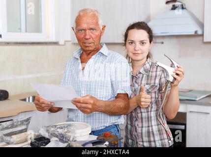 Happy woman with father discussing work manual on mixer tap Stock Photo
