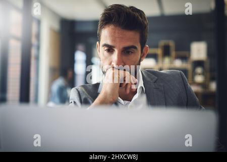 He is a big thinker. Shot of a focused young businessman working on his laptop while contemplating inside of the office. Stock Photo