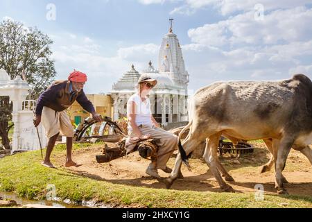 A farmer gives a tourist a ride as he draws water from a well by a wheel turned by bullocks for irrigation, Kumbhalgarh, Rajsamand district, Rajasthan Stock Photo