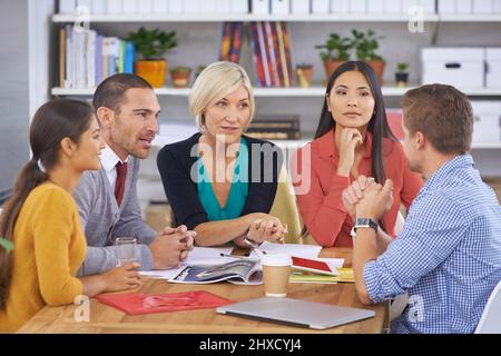 Hanging on his every word. A group of businesspeople talking while sitting around a table. Stock Photo