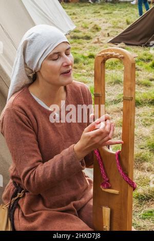 England, East Sussex, Battle, The Annual Battle of Hastings 1066 Re-enactment Festival, Female Participant Dressed in Medieval Costume Playing Medieval Stringed Wooden Musical Instrument Stock Photo