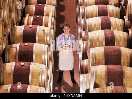 Surrounded by all of his hard work. Portrait of a young wine maker standing with his barrels of red wine.