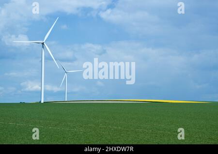 Rural landscape in France with blue sky and green field with spinning wind power stations producing environmentally friendly electric energy. Stock Photo