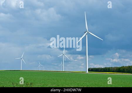 Rural landscape in France with blue sky and green field with spinning wind power stations producing environmentally friendly electric energy. Stock Photo