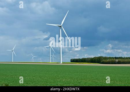 Rural landscape in France with blue sky and green field with spinning wind power stations producing environmentally friendly electric energy. Stock Photo