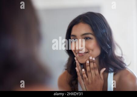 Your face will show you inner glow. Shot of a beautiful young woman admiring herself in the mirror at home. Stock Photo