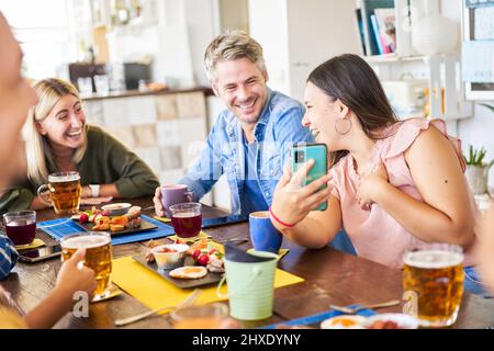 Group of young couple friends with phones smiling in a cafe bar. Having drink - food and watching mobile. Stock Photo