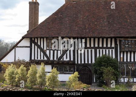 Black and white timbre structured building with leaded windows and a large roof made of small red tiles and a black arched doorway Stock Photo