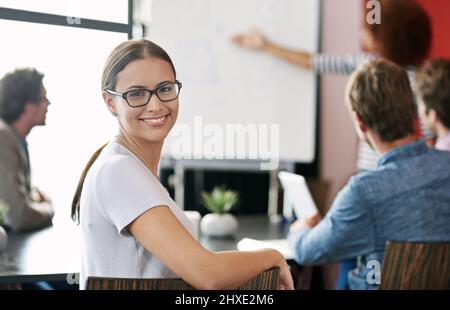 My team makes success look easy. Portrait of a young office worker in a meeting with colleagues in the background. Stock Photo