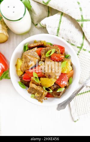 Beef with oranges, bell pepper and ginger root in bowl, towel and fork on wooden board background from above Stock Photo