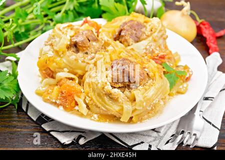 Twisted pasta with meatballs in the center with cream sauce, stewed tomatoes, bell peppers, onions and garlic in white plate on dark wooden board back Stock Photo