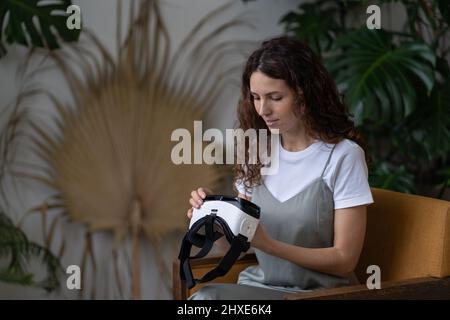 Young female gardener or plant shop owner testing with virtual reality glasses in greenhouse Stock Photo