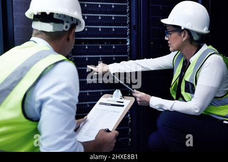 The more you know the more you grow. Shot of two technicians working together in a server room. Stock Photo