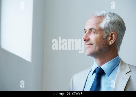 Time for business. Shot of a thoughtful-looking mature businessman looking out of a window. Stock Photo