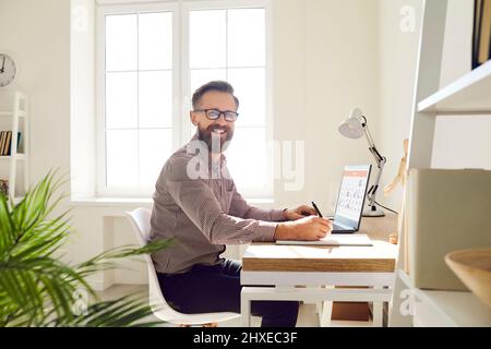 Happy businessman sitting at office desk, using calendar on laptop and planning working schedule Stock Photo