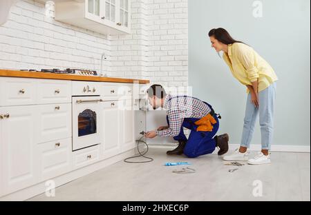 Plumber cleaning clogged pipes under the kitchen sink with the help of a drain cable Stock Photo