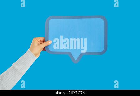 Anonymous woman holding blank blue paper mockup message bubble on blue background Stock Photo