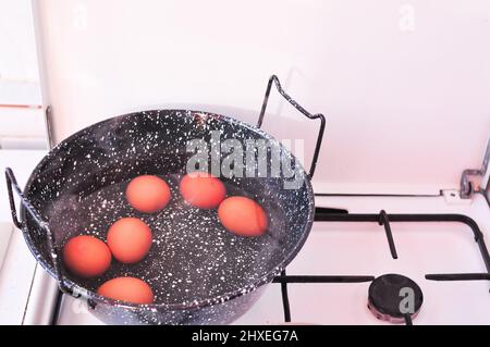 Eggs in shell in boiling water in black pot on the stove . High quality photo Stock Photo