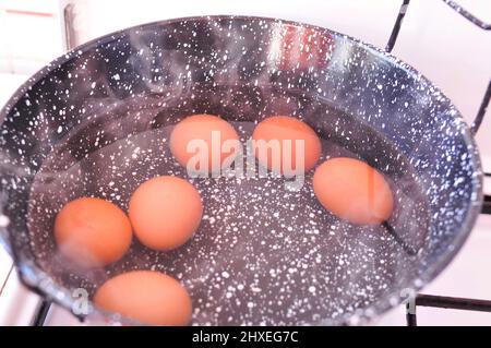 Eggs in shell in boiling water in black pot on the stove . High quality photo Stock Photo