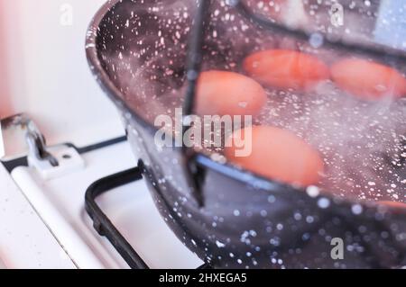 Eggs in shell in boiling water in black pot on the stove . High quality photo Stock Photo