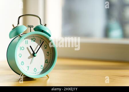 Alarm clock in the morning on the table in the bedroom against the background of the window with the morning bright sun. Wake up, time, new day, optimism concept. High quality photo Stock Photo