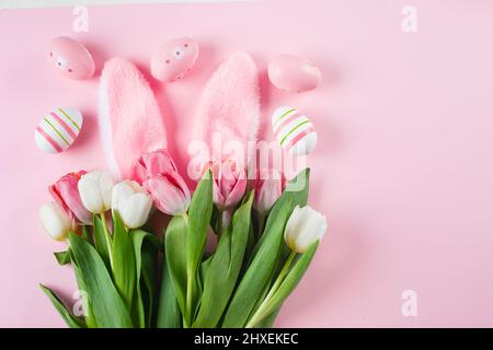 Easter funny composition. Pink background with tulips, easter eggs, fluffy bunny ears. Flat lay, top view Stock Photo