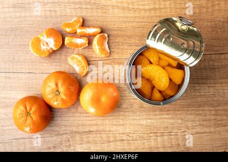 Canned tangerine. Pickled mandarin fruit in the can on wooden table. Top view. Stock Photo