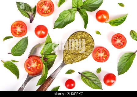 Mix of slice of tomatoes, basil leaves and vintage spoons with green pesto isolated on white background Stock Photo