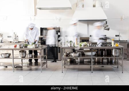 Chef cooks working in professional kitchen. Chefs hurry up, actively cooking meals for restaurant. Long exposure with motion blurred figures Stock Photo