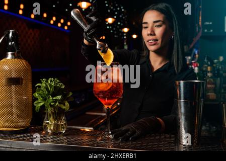 The young Latin brunette prepares a cocktail at the bar counter. job waitress profession Stock Photo