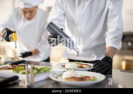 Multiracial group of cooks finishing main courses while working together in the kitchen. Team prepares meals for the restaurant  Stock Photo
