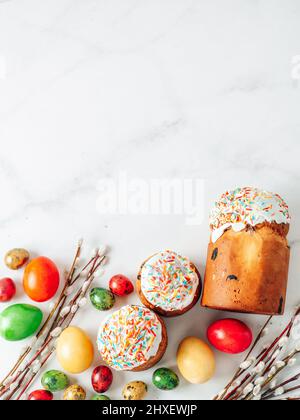 Traditional Russian Ukrainian Easter Cake Kulich. Orthodox Christian Easter Bread or Easter Cake with frosting, Easter Eggs and willow twigs on white marble background. Copy space. Flat lay. Vertical Stock Photo