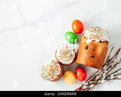 Traditional Russian Ukrainian Easter Cake Kulich. Orthodox Christian Easter Bread or Easter Cake with frosting, Easter Eggs and willow twigs on white marble background. Copy space. Flatlay or top view Stock Photo