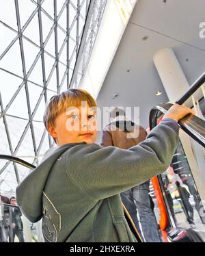 child on moving staircase looks self confident and smiles Stock Photo