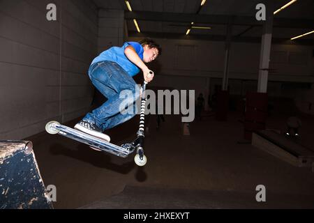 boy with scooter is going airbornein the skate hall Stock Photo