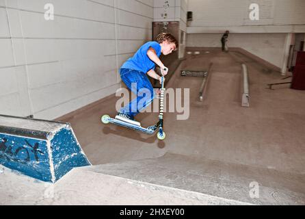 boy with scooter is going airborne in the skate hall Stock Photo