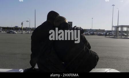 Young gay male couple sitting on a bench at bus stop, talking, and hugging. HDR. Two men in love waiting for a bus outdoors during conversation on a Stock Photo