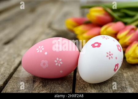 Two Easter eggs and a bouquet of tulips on a rustic wooden table. Selective focus. Stock Photo