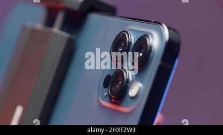 Russia - Moscow, 09.28.2021: extreme close up of cameras of a new Iphone 13 pro max fixed by steadicam. Action. New smartphone isolated on purple wall Stock Photo