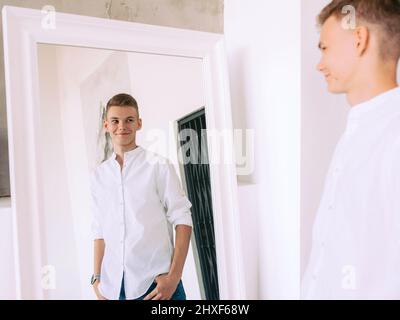 handsome guy in white shirt and blue jeans standing by the mirror indoor. Fashion, style concept Stock Photo