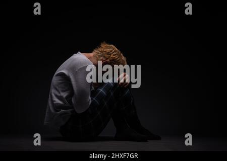 sad and depressed boy is sitting on the ground while crying on his own Stock Photo